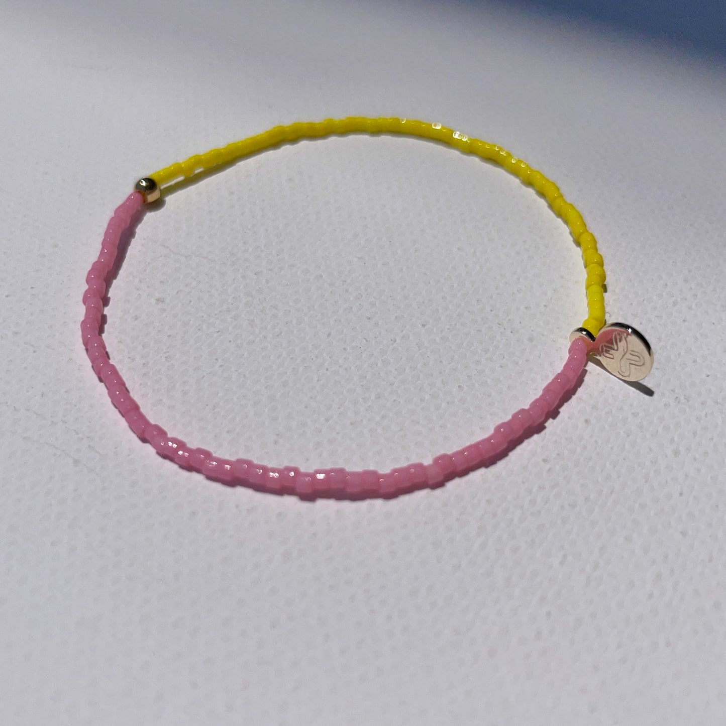 B-Color bright Yellow and Pink beaded bracelet with gold plated detail and an engraved gold tone STRIPE+BEAT plus charm