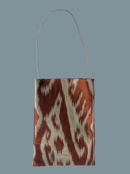 A small rectangular shoulder bag with a thin shoulder strap, featuring a brown and cream ikat pattern.