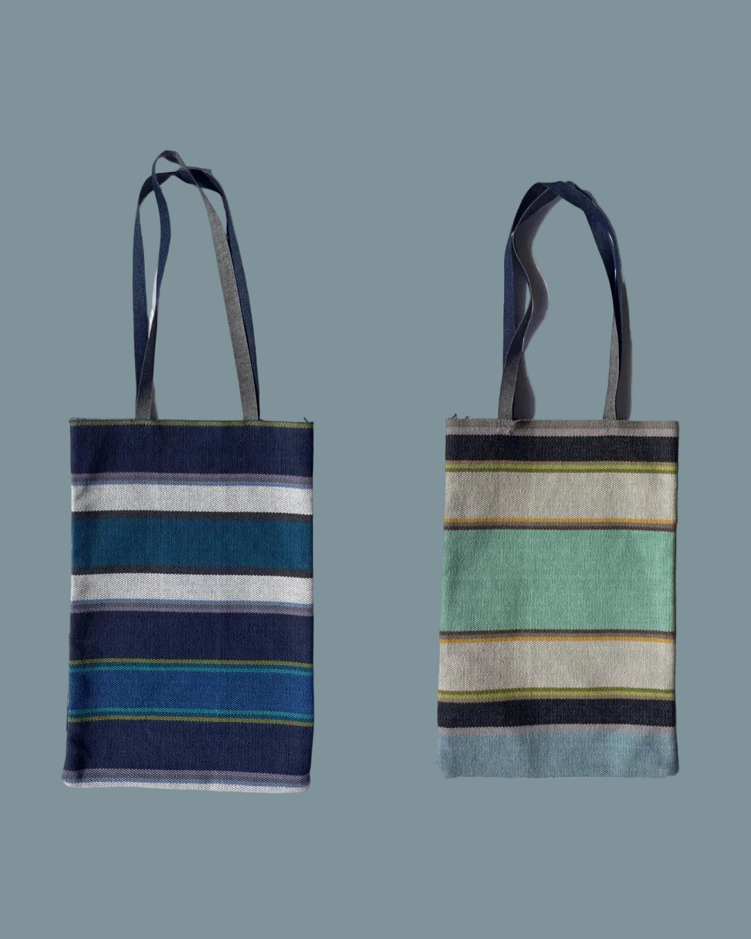 striped woven tote bag with denim handles. One side is navy, teal, blue, and white stripes, while the other features mint green, beige, navy, and light yellow stripes.