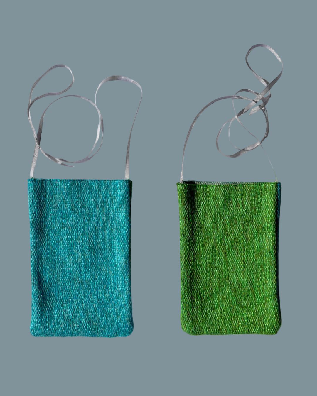 Two small woven shoulder bags shown side by side on a white fabric background, one in teal-blue and one in bright green, both with thin gray straps.