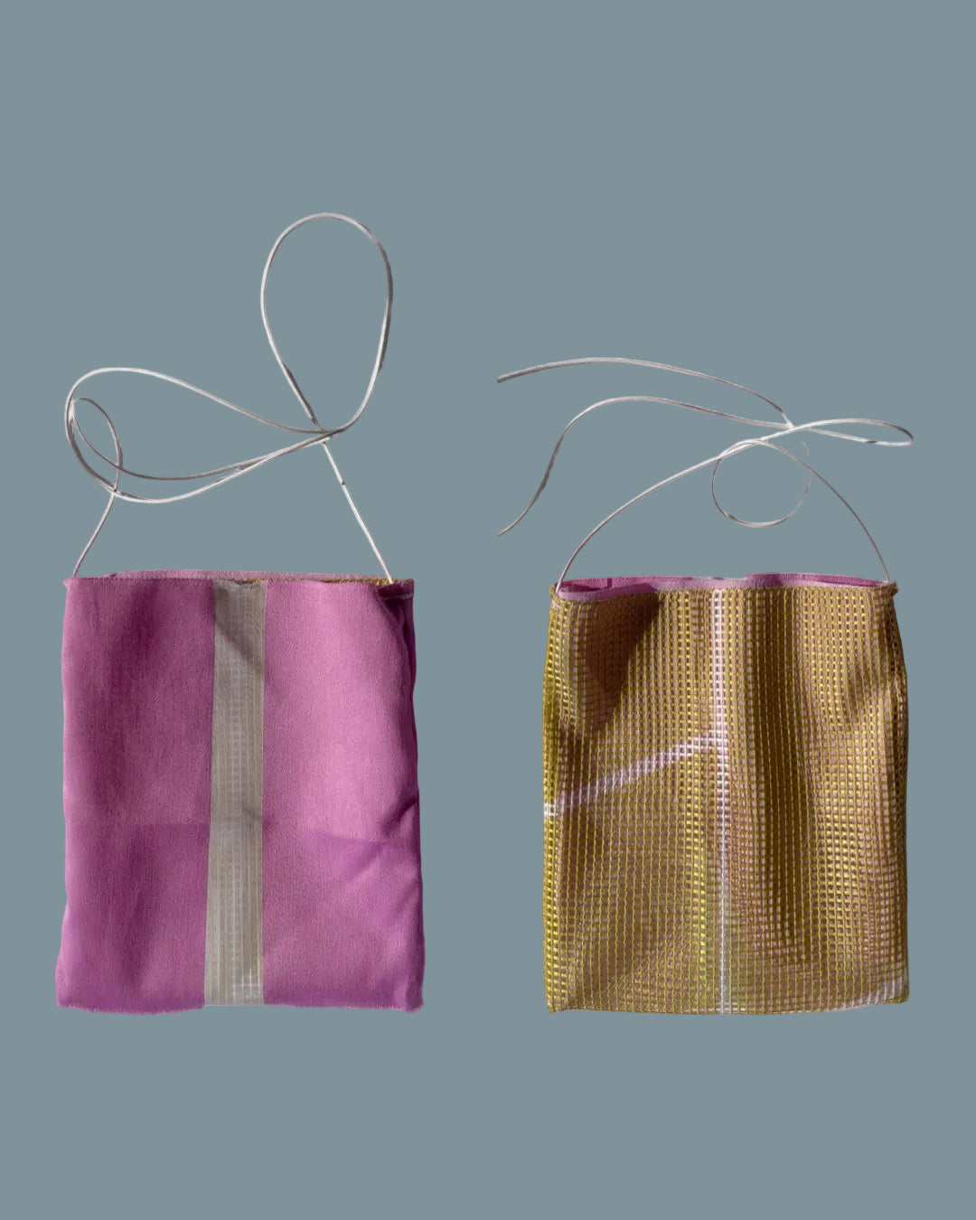 Two small mesh drawstring pouches or bags shown side by side on a wrinkled white fabric background. The left pouch is solid pink with a vertical white stripe, and the right pouch is metallic gold with a white stripe.