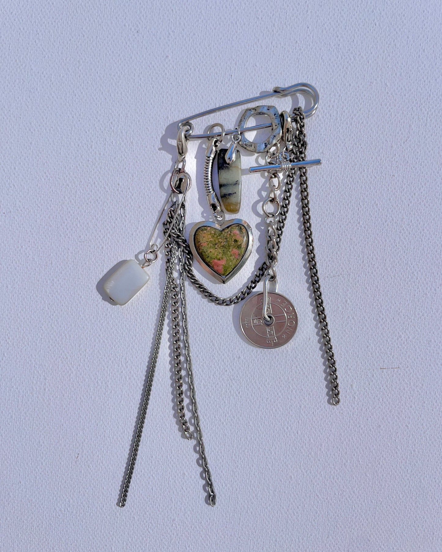 Keepsake objet trouvé safety pin with multiple charms, coins and objects attached to it.