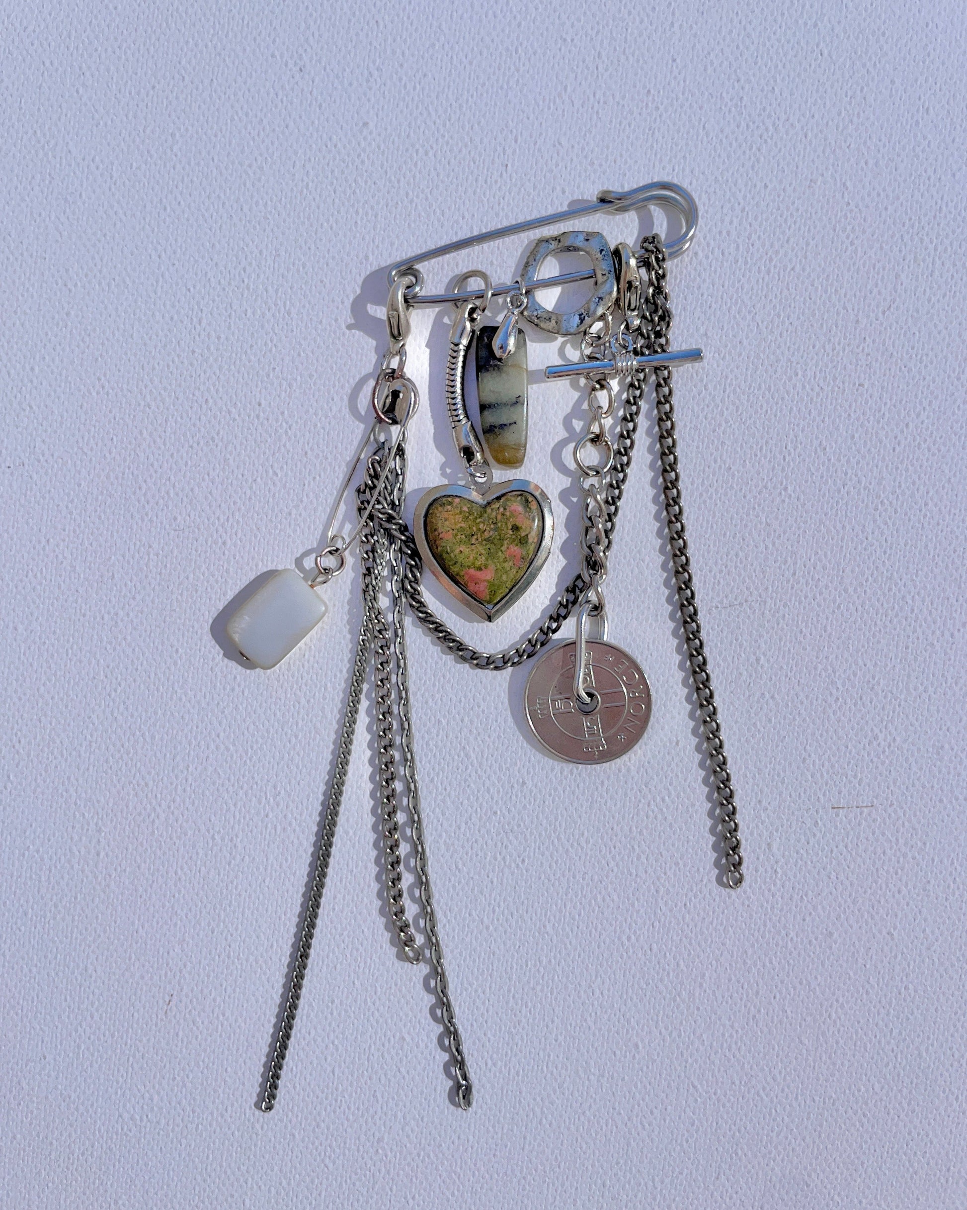 Keepsake objet trouvé safety pin with multiple charms, coins and objects attached to it.