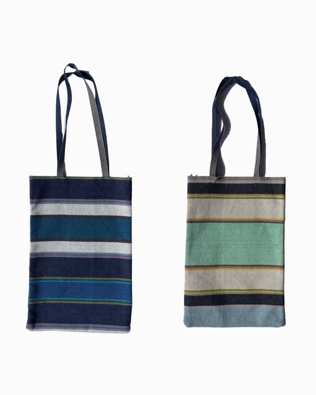 striped woven tote bag with denim handles. One side is navy, teal, blue, and white stripes, while the other features mint green, beige, navy, and light yellow stripes.