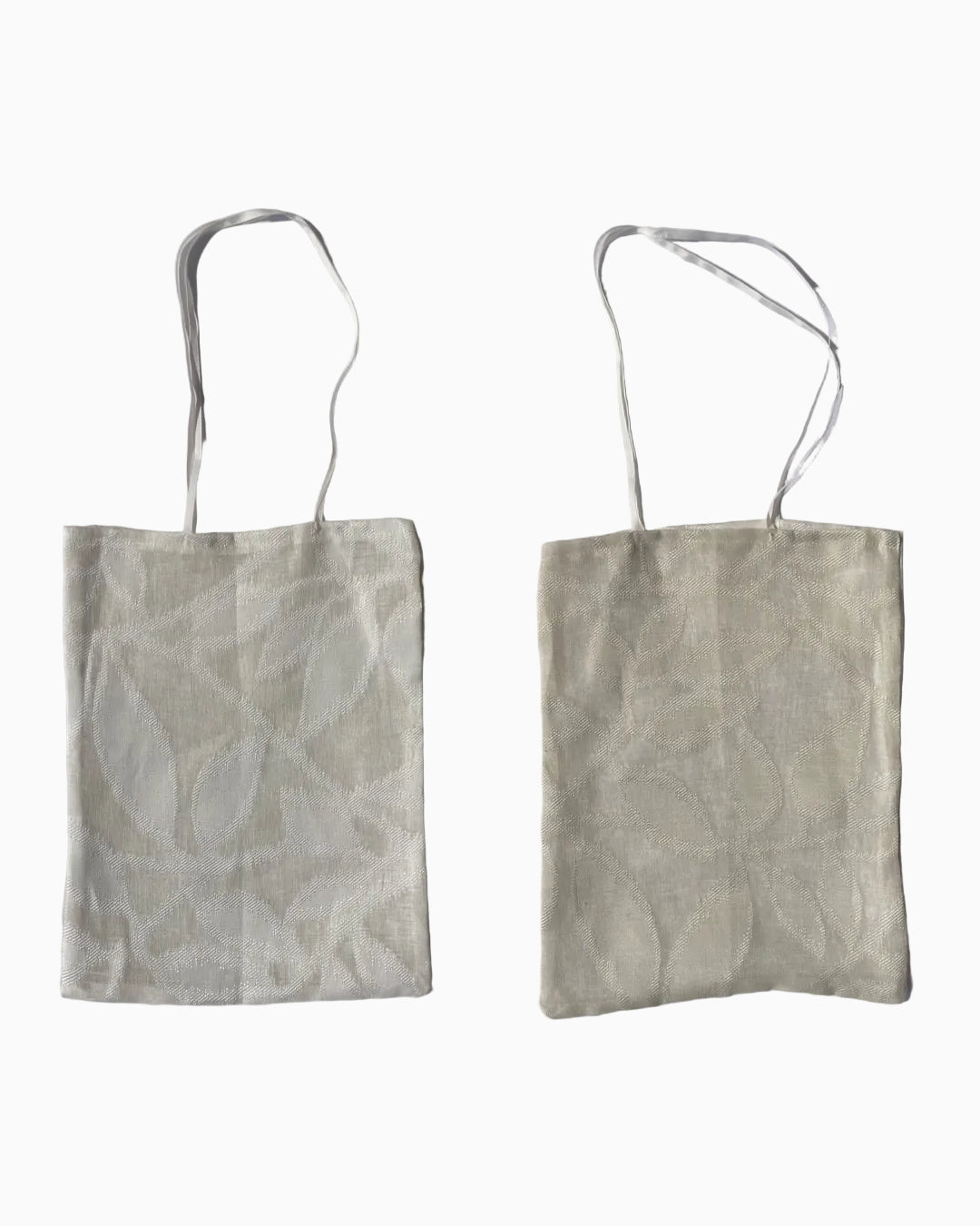 Two views of a white and cream-colored see through woven linen fabric tote bag with a subtle leaf pattern and white gross-grain ribbon handles.